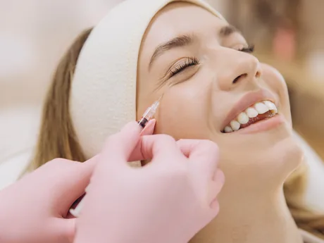 A smiling woman receiving a facial injection treatment