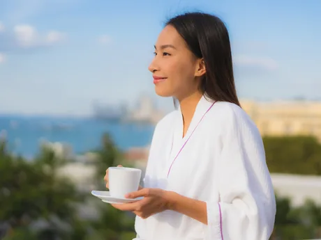 A woman holding a warm mug, looking out at the morning