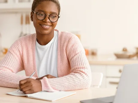 A woman taking notes during a video consultation at home