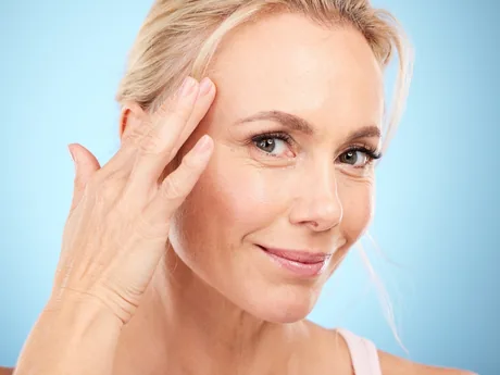 A woman in her fifties touching her cheek, smiling